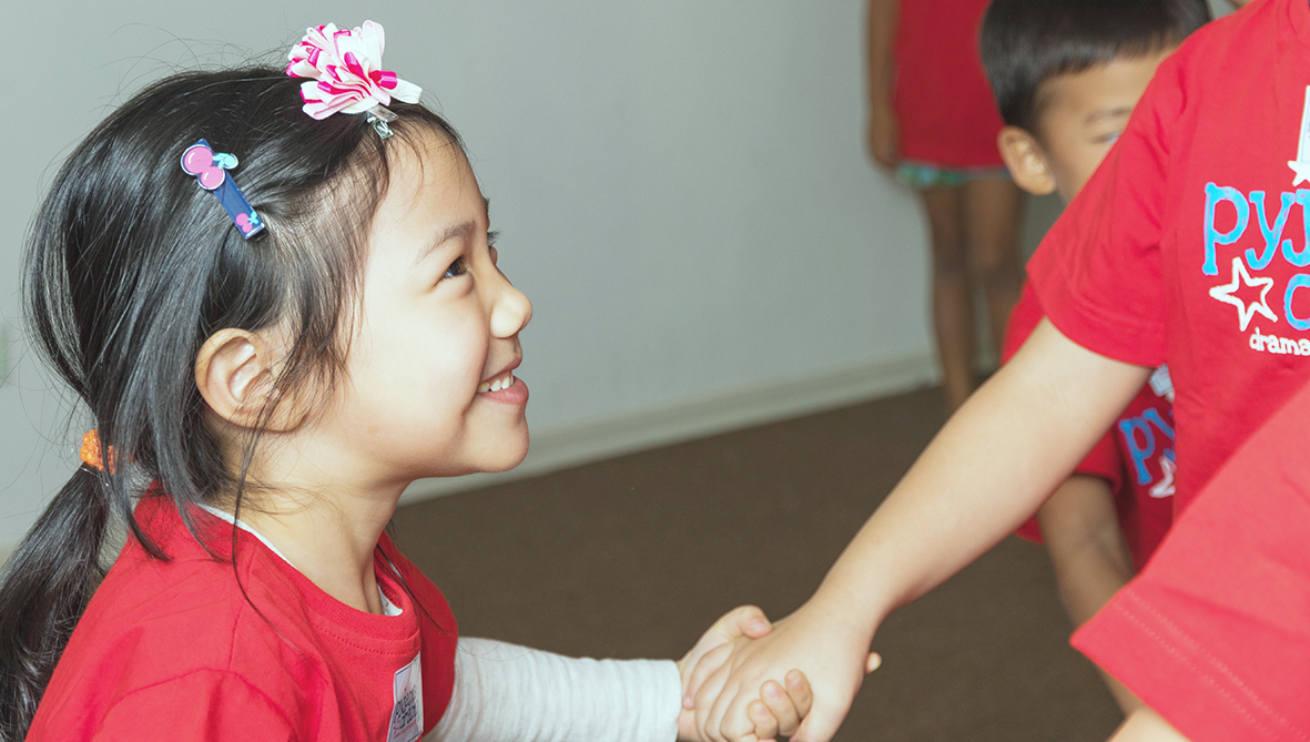 Girl in a class in Malaysia smiling and holding the hand of another child.